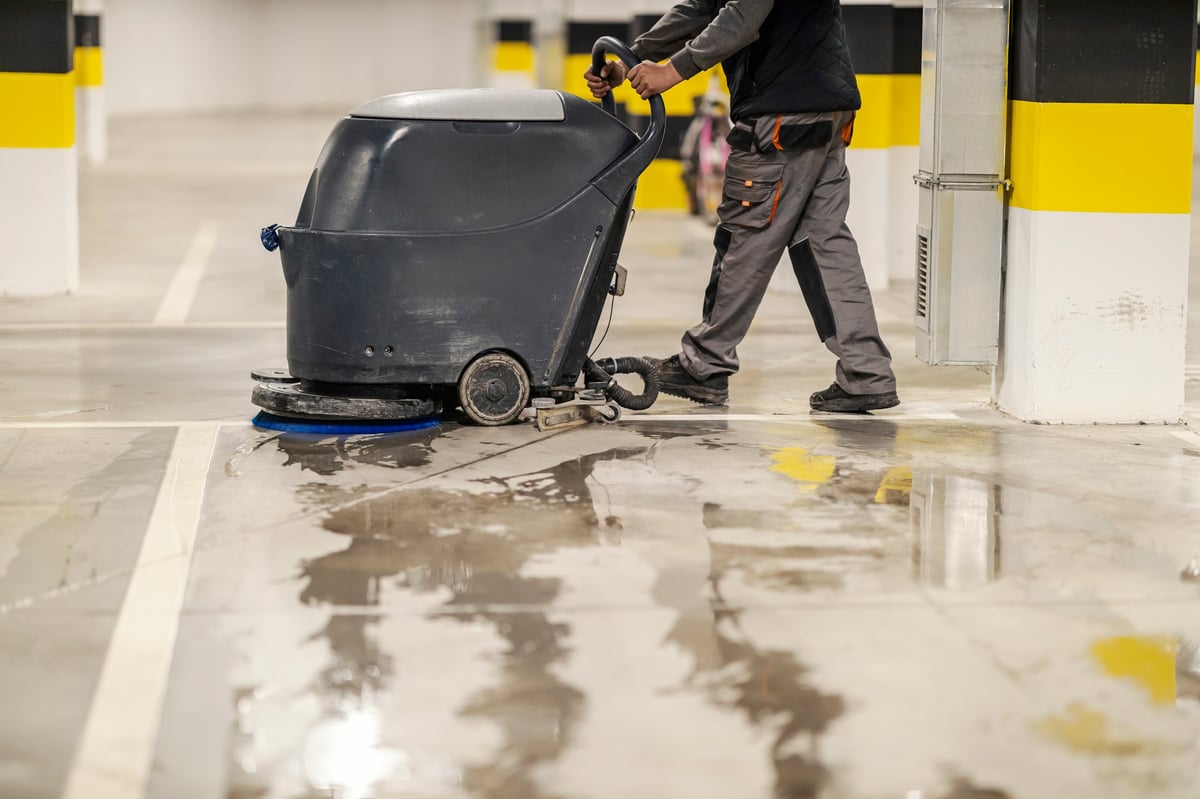 Professional worker washing garage parking floor with industrial cleaning machine — commercial-grade results